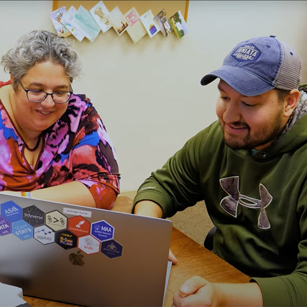 Nick and Professor Kim Roth sit together at a table and look at data on a laptop. 