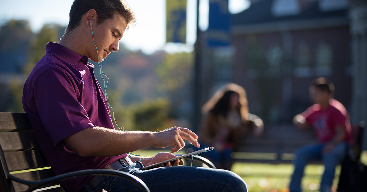 student using a tablet on a park bench
