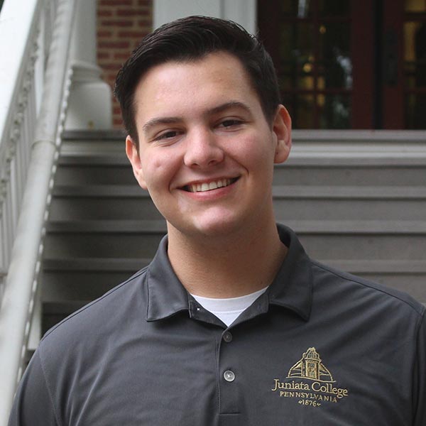 Owen stands in front of the Founders Hall staircase