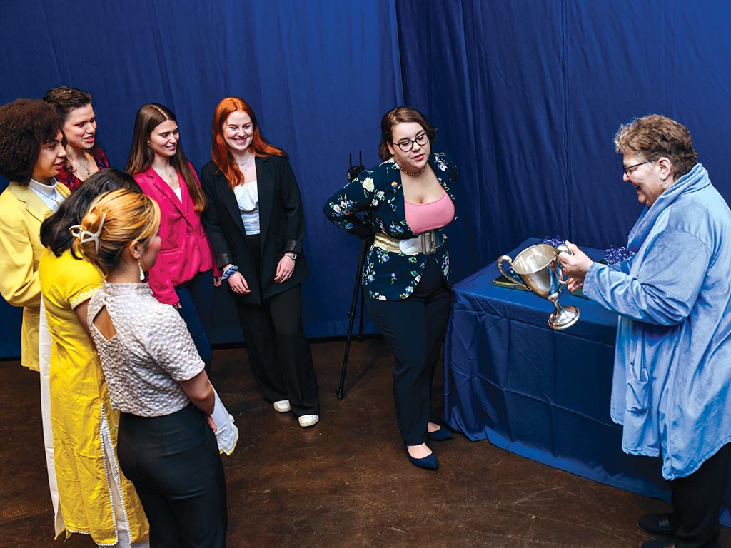 Donna Weimer, Thornbury Professor of Communication, right, showed the antique silver loving cup to the seven finalists, clockwise from the left, Nhu “May” Nguyen ’23, Kiran Patil ’24, Kayla Blackstock ’23, Molly Sheets ’26, Lillian Case ’25, Hannah Kempken ’23, and Elizabeth Bailey ’23.